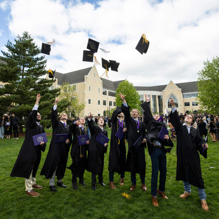 students throwing grad caps in air on lower quad