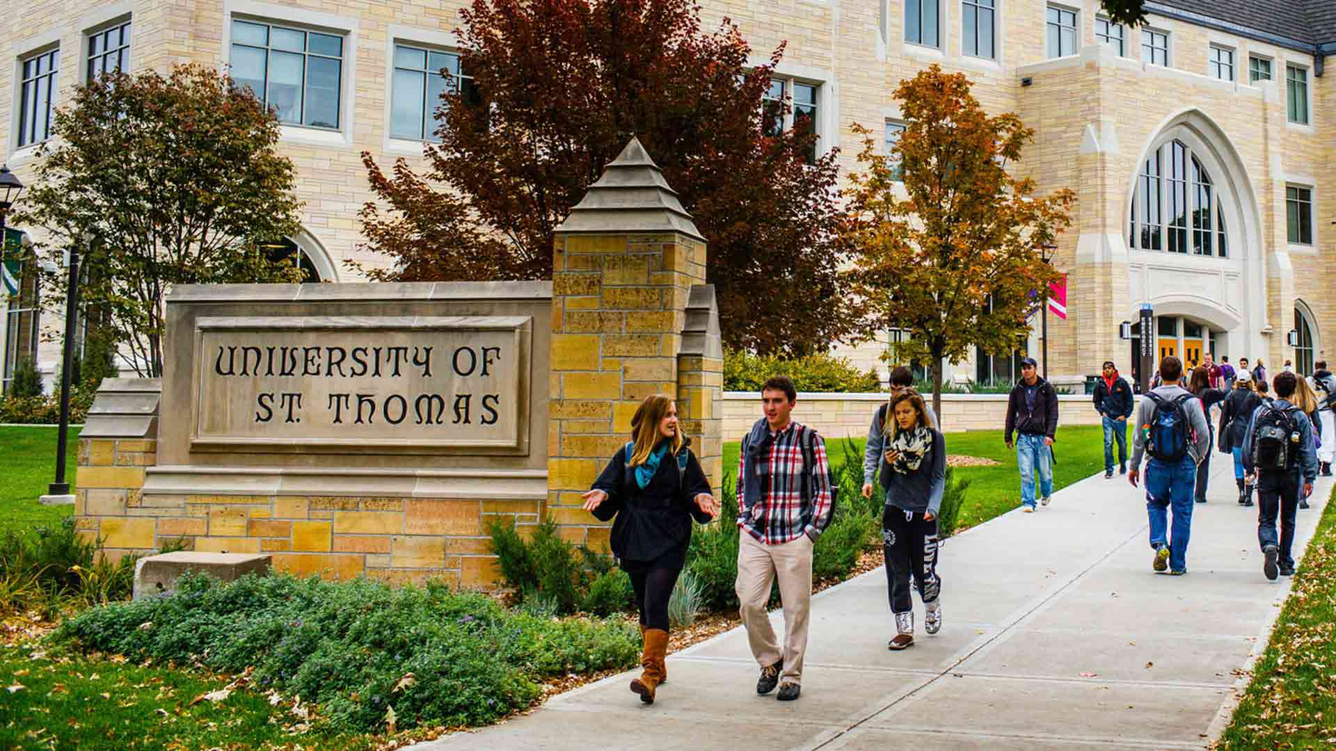 Students walk past a "University of St. Thomas" monumental sign.