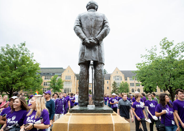 students in purple shirts walk by a status of John Ireland
