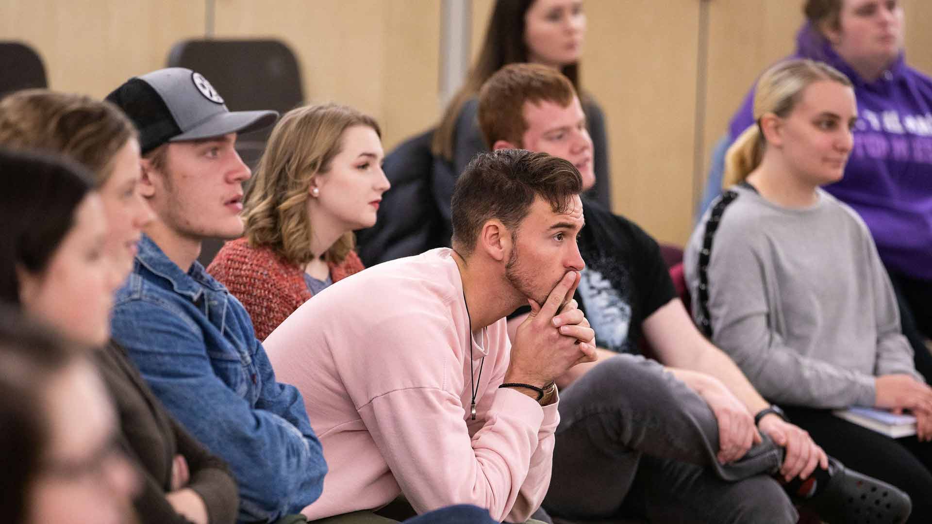 Male student in crowd watches presentation.