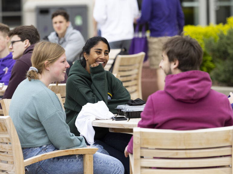 Three students sitting at an outdoor table smiling.