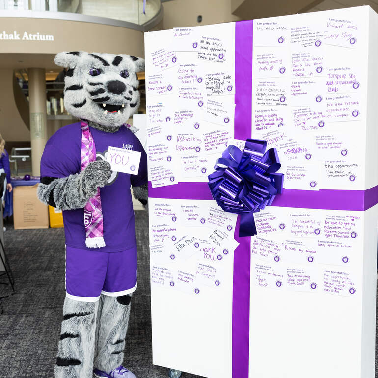 tommie mascot stands beside a board made to look like a present, with notes of gratitude on it