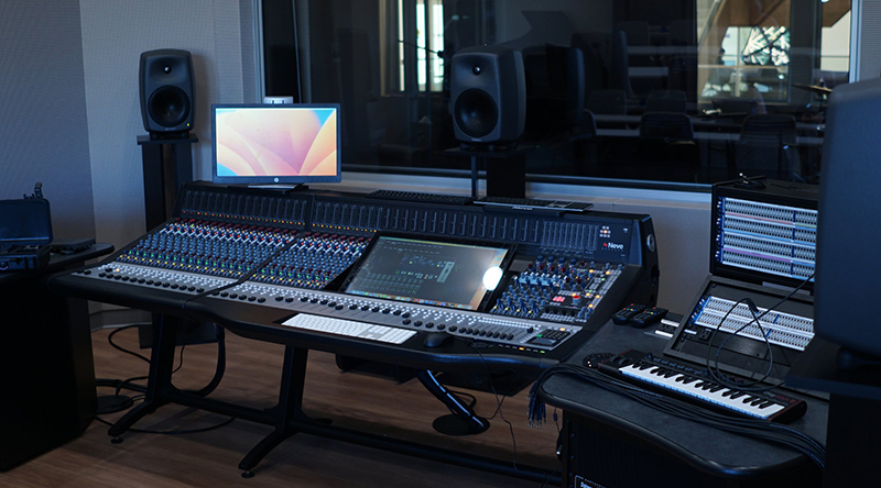 Recording studio at Schoenecker Center. Large console with many knobs and buttons, separated by a glass wall from a live instrument space.