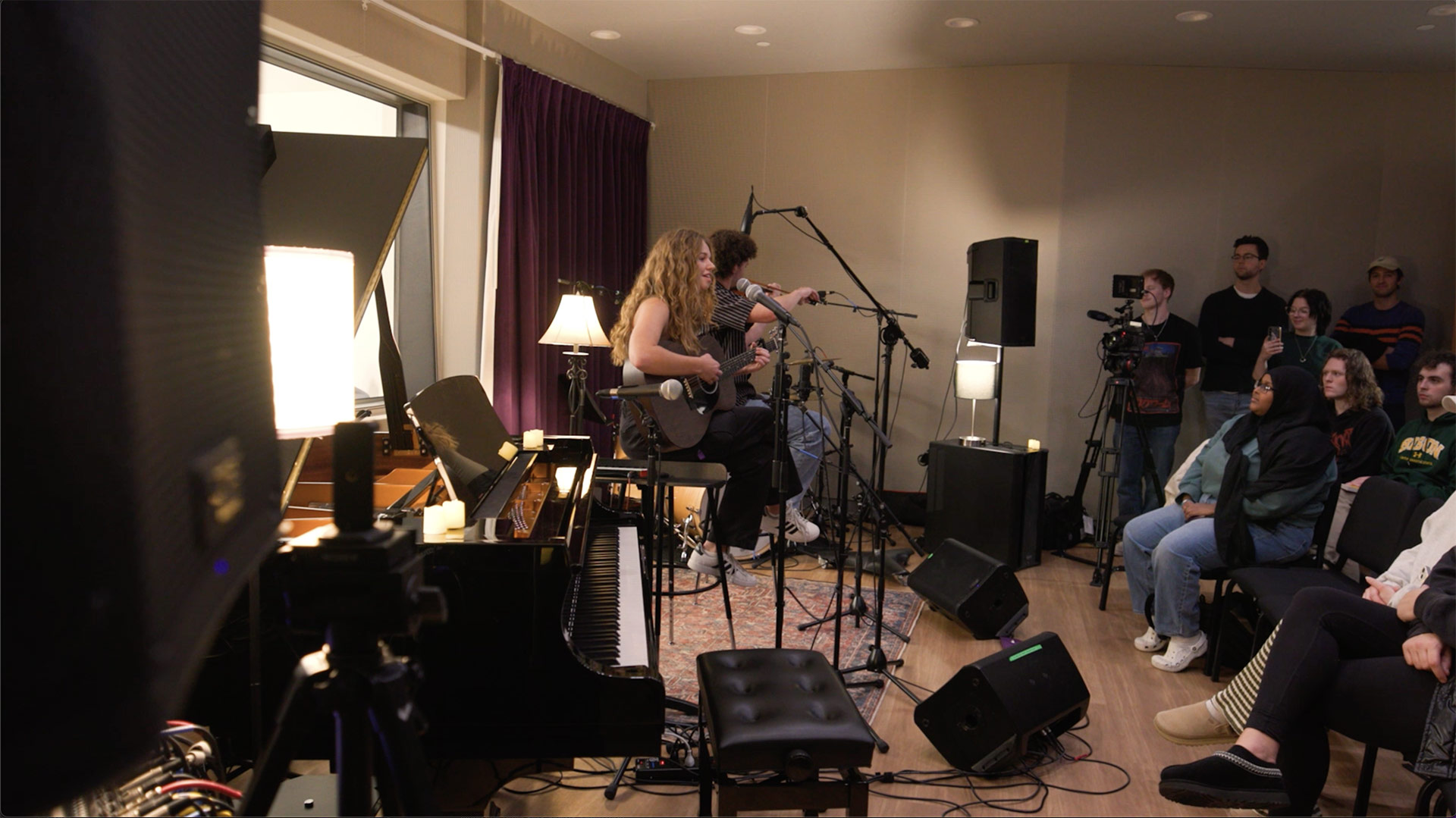 An acoustic guitarist and violinist play to a small crowd gathered in the Schoenecker Center recording studio