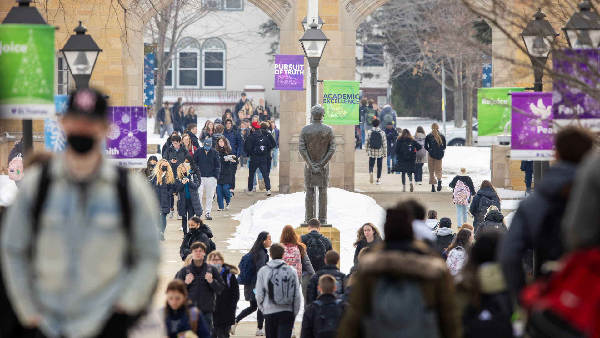 students walking through the center of the quad with John Ireland, the Arches and “Pursuit of Truth” and “Academic Excellence” flags prominently displayed