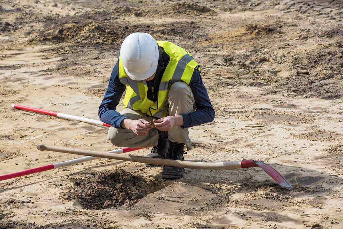 Person in hardhat and hi-vis vest examines soil at a construction site.