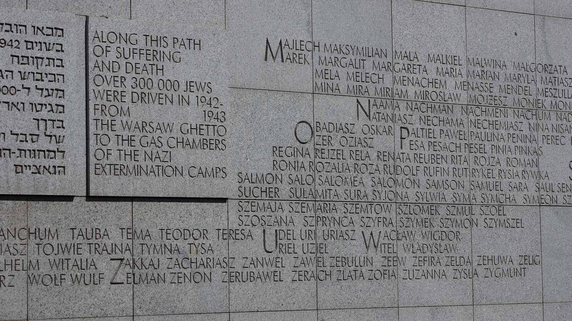 Photo of the Memorial to the Warsaw Ghetto featuring a grey concrete wall with the names of many Jewish victims