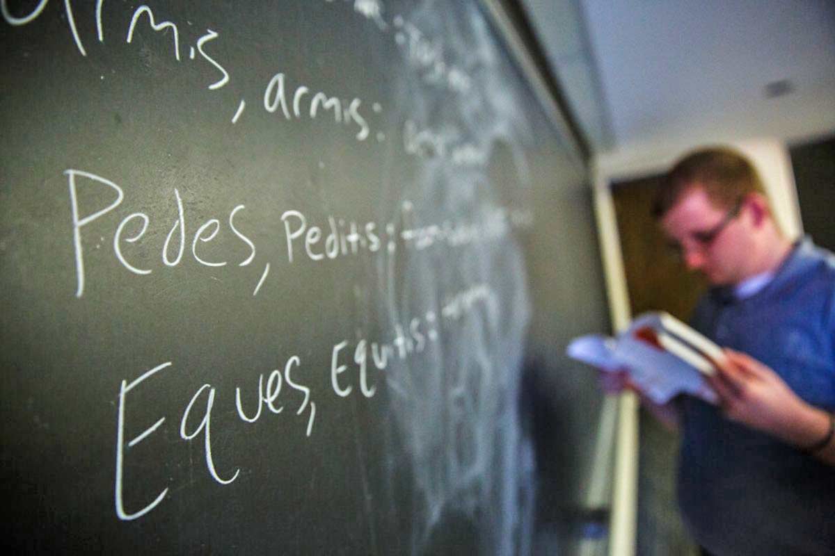 A student writes in Latin on a chalkboard.