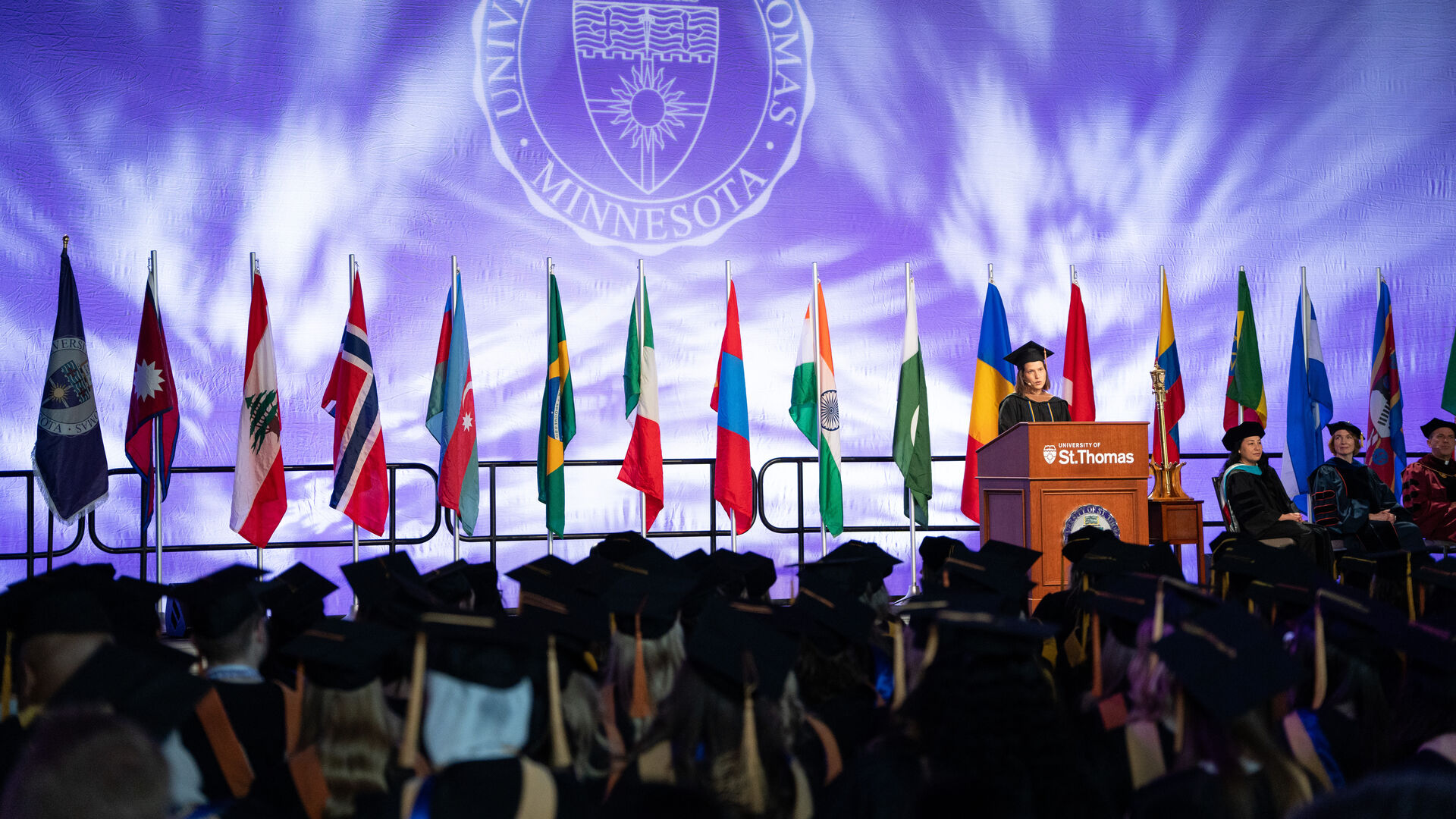 large group of St. Thomas students in graduation robes throwing cap in the air