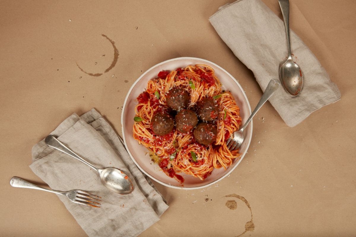 Bowl of spaghetti on kraft tablecloth with used silverware on grey cloth napkins