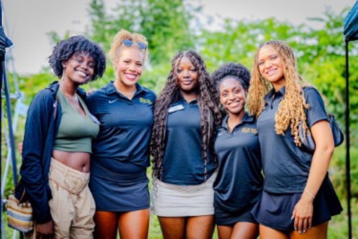 Group of five women with arms around one another and smiling
