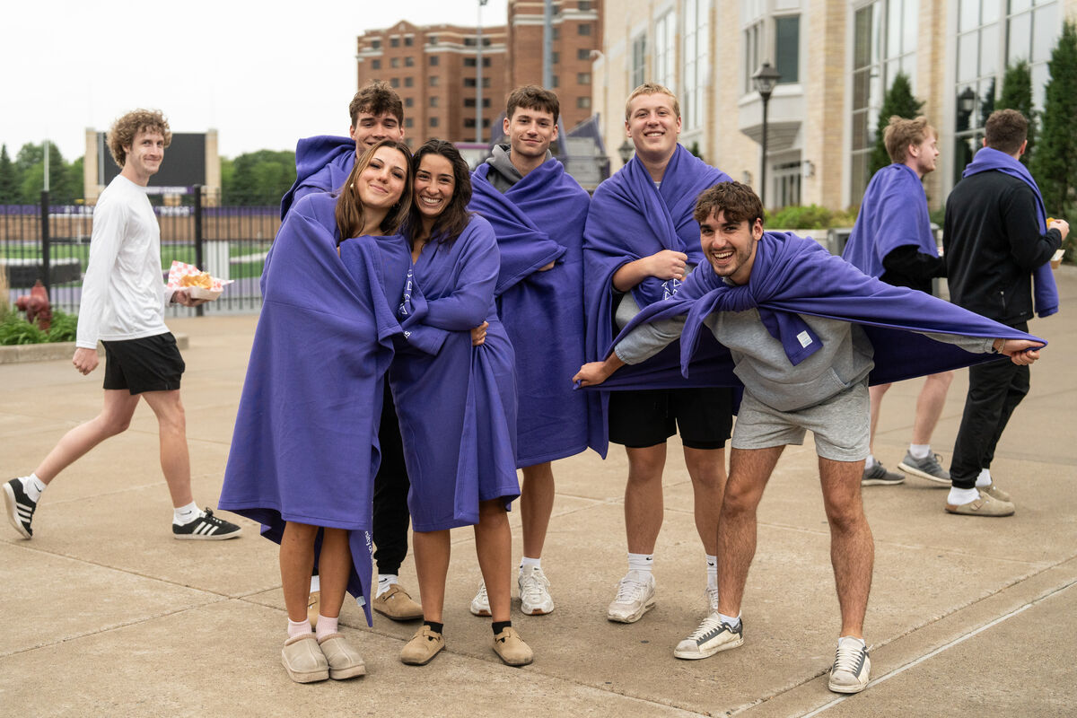 group of students wearing purple blankets pose outside