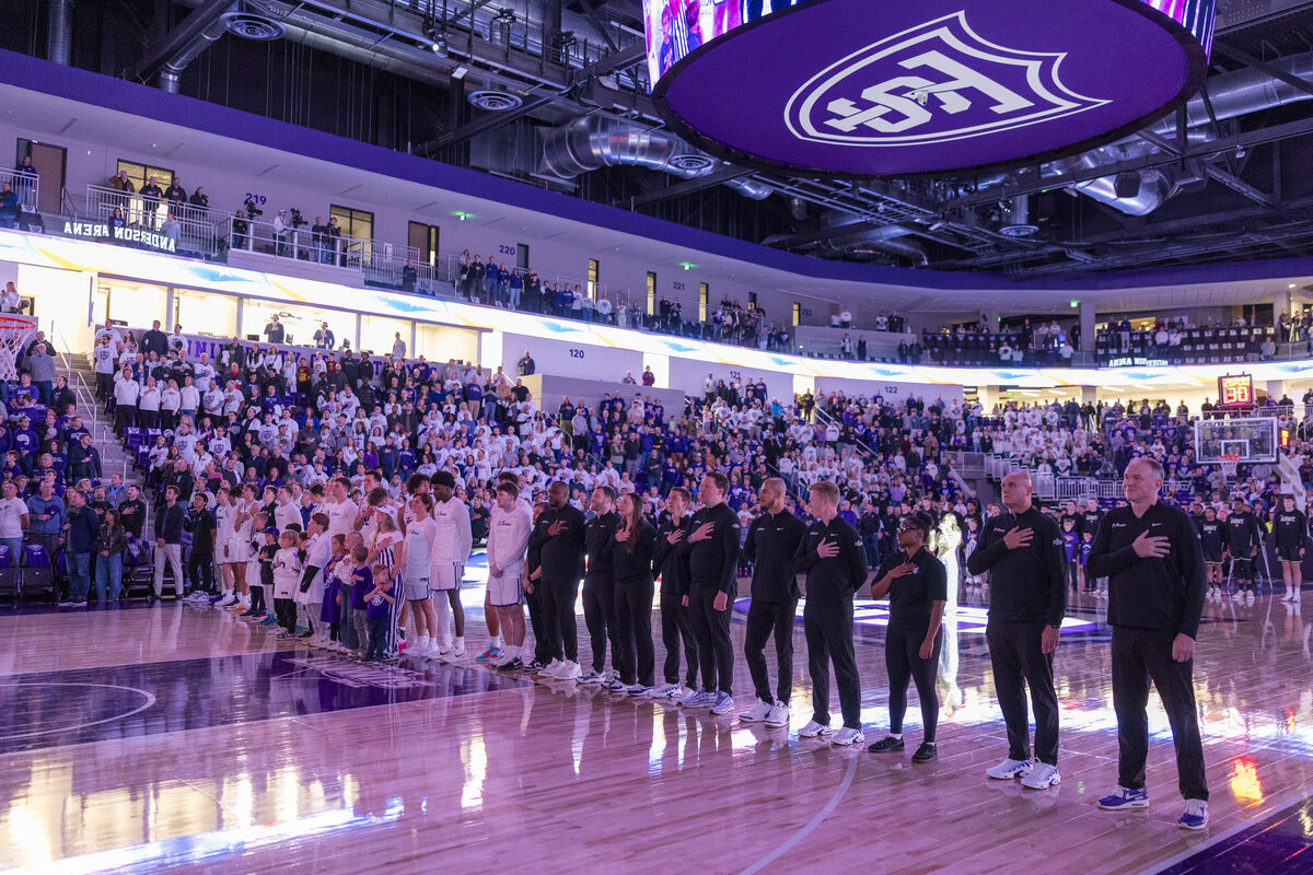 people on the basketball court hold their hands over their hearts during the pledge of allegiance