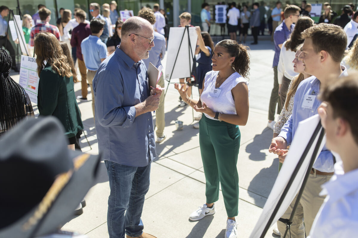 student outside explains a poster concept to a professor with group nearby