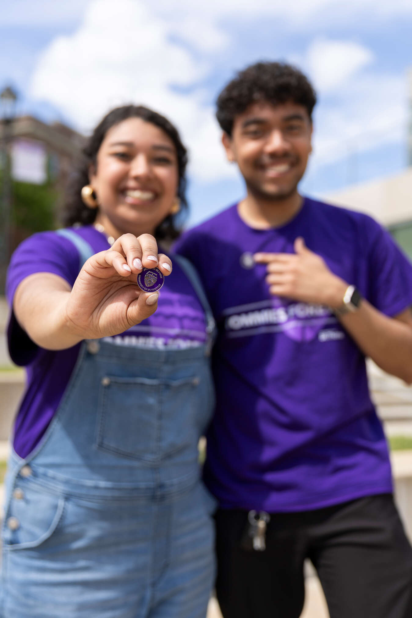 two students holding out their first-generation college graduate pin and smiling.