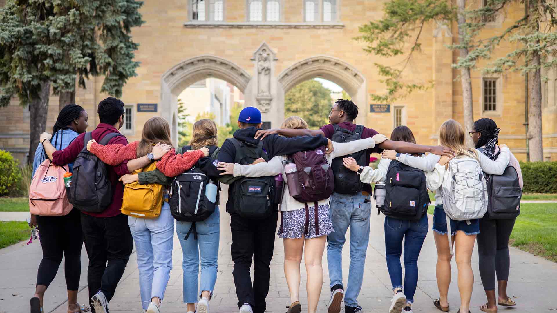 Students embracing and walking toward arches