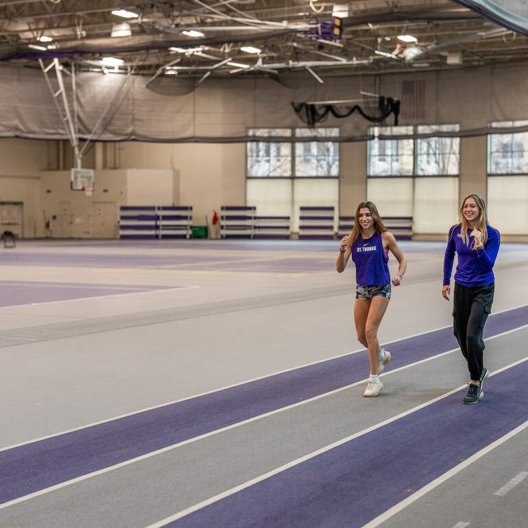 two students running on the indoor track at the university of st thomas