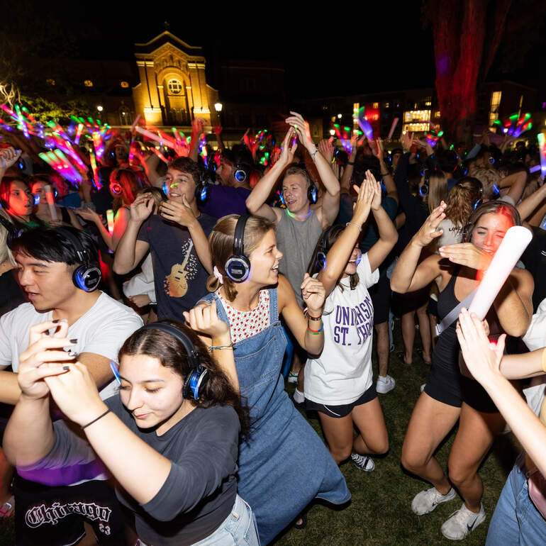 Students dancing outside at night wearing headphones