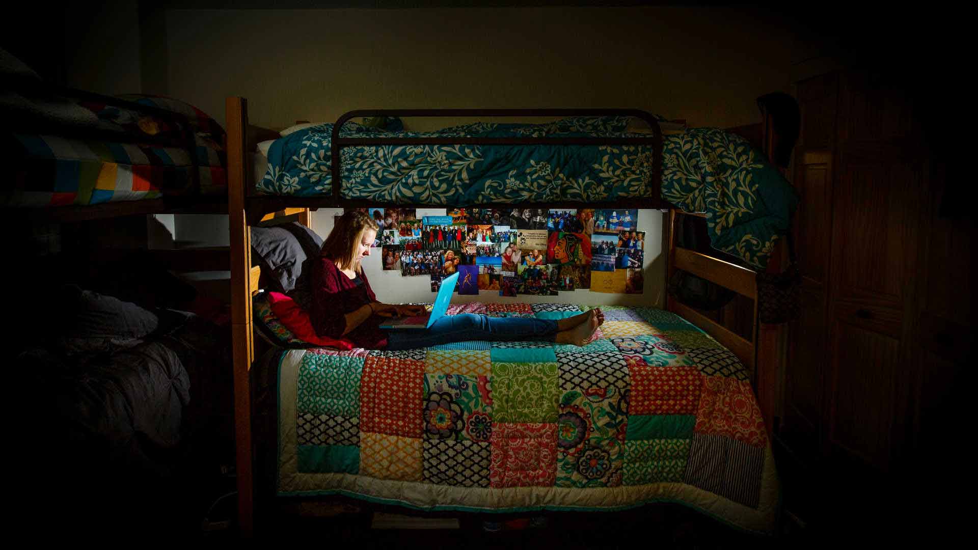 student works on laptop on the bottom bunk