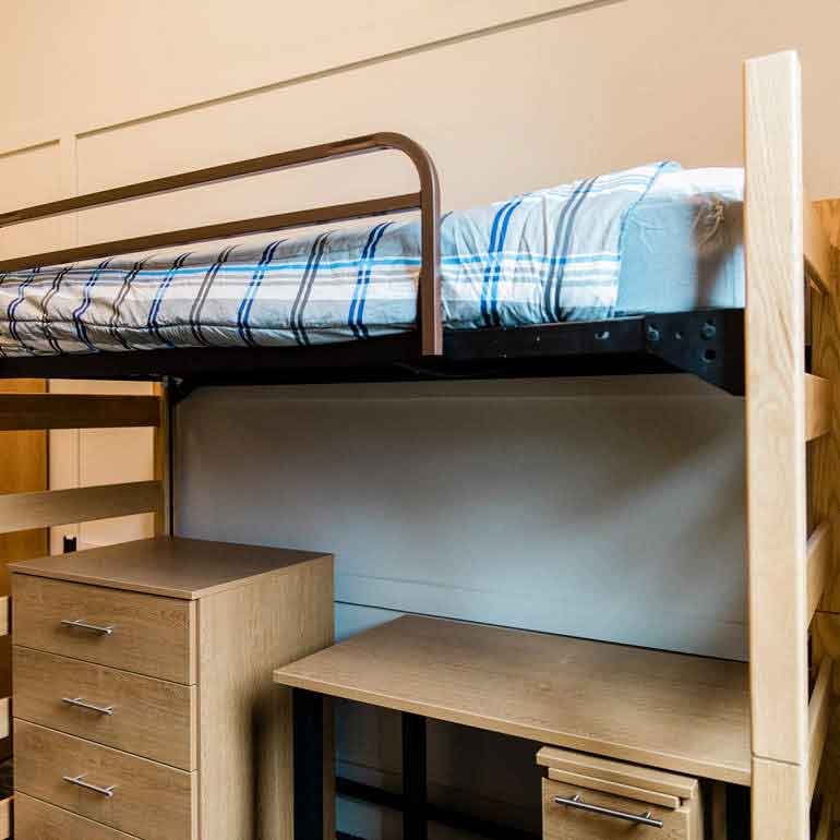 Dorm room with lofted bed over a desk and set of drawers.