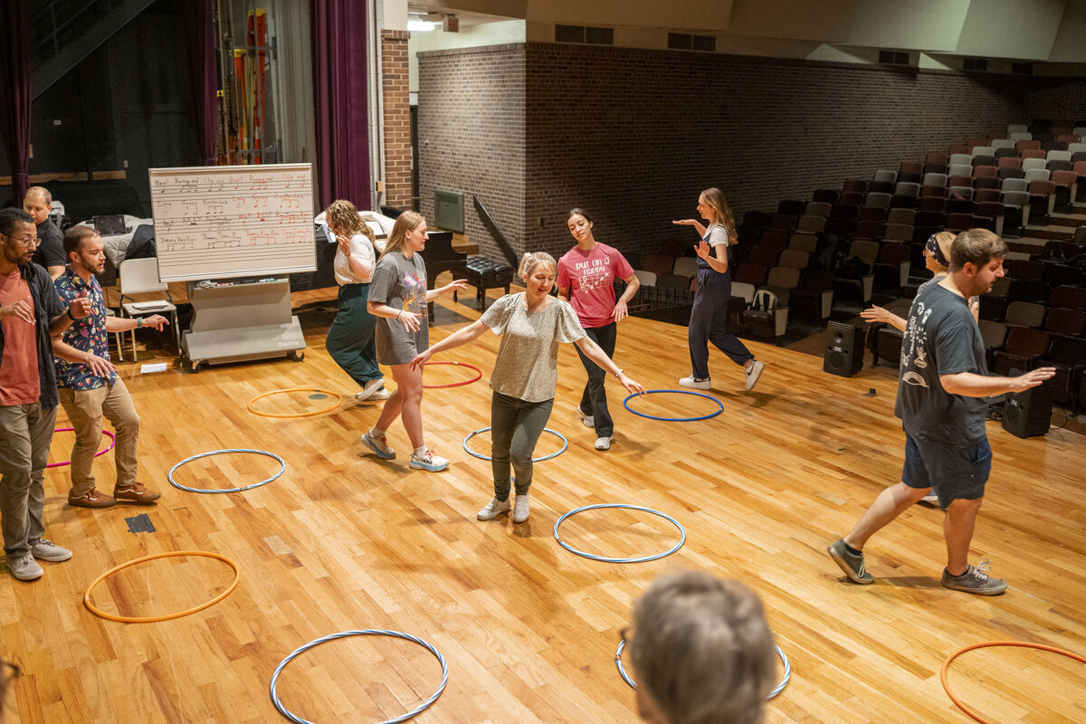 Students on an auditorium stage moving around hula hoops