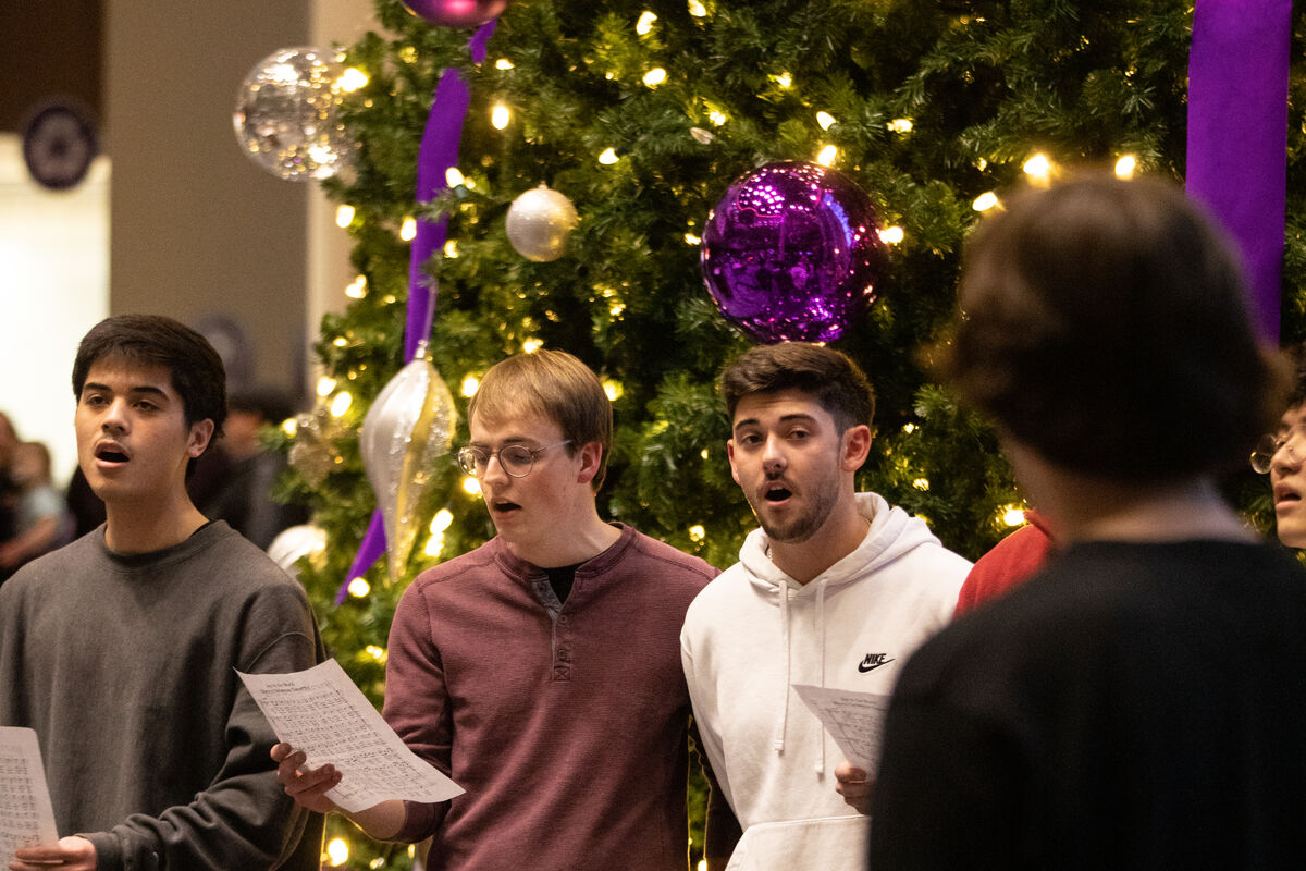 Carolers sing in front of the large Christmas tree with purple ornaments